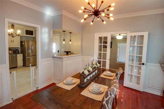 dining room featuring crown molding, light wood finished floors, wainscoting, and an inviting chandelier