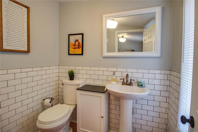 half bath featuring a wainscoted wall, a sink, tile walls, and toilet