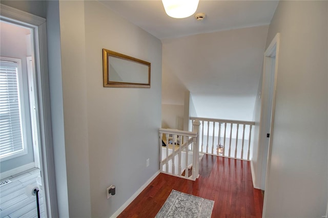 corridor with baseboards, an upstairs landing, and wood finished floors