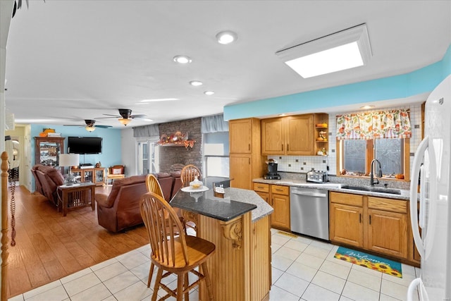 kitchen featuring light tile patterned floors, a kitchen island, a sink, stainless steel dishwasher, and freestanding refrigerator