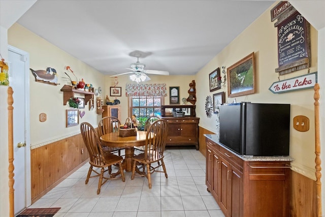 dining space featuring light tile patterned floors, wood walls, wainscoting, and a ceiling fan