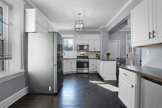 kitchen featuring white cabinetry, ornamental molding, appliances with stainless steel finishes, dark countertops, and dark wood finished floors