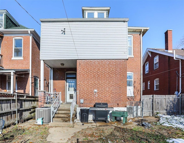 rear view of house with central AC, brick siding, and fence