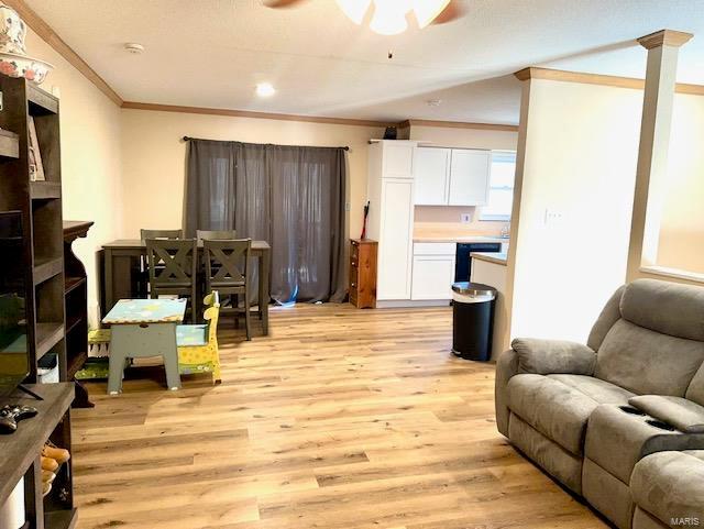 living room featuring light wood finished floors, ceiling fan, ornamental molding, and ornate columns