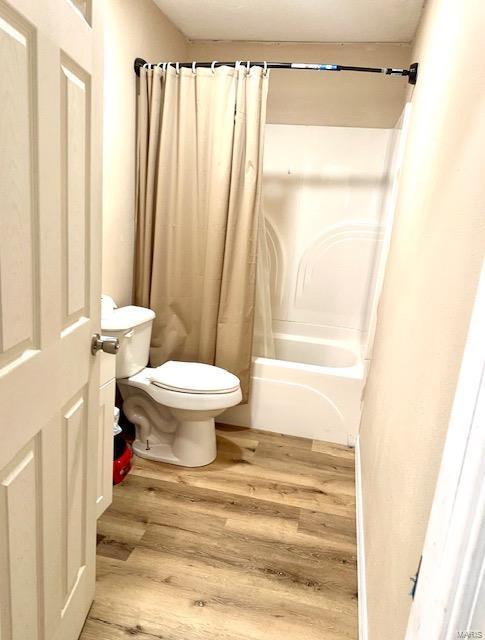 bathroom with toilet, shower / bath combo with shower curtain, and wood finished floors