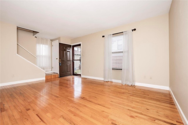 empty room featuring light wood-type flooring, a wealth of natural light, stairway, and baseboards