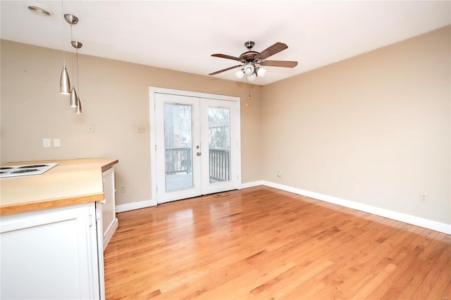 unfurnished dining area featuring french doors, light wood-type flooring, a ceiling fan, and baseboards