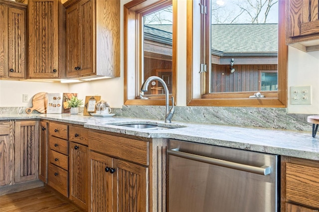 kitchen with dishwasher, a sink, brown cabinets, wood finished floors, and light stone countertops