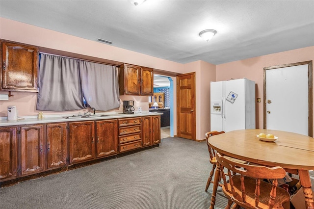 kitchen with light countertops, white refrigerator with ice dispenser, a sink, and visible vents