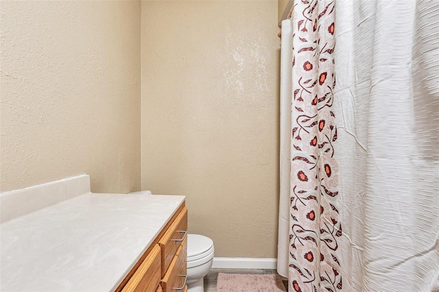 bathroom featuring a textured wall, toilet, vanity, baseboards, and a shower with curtain