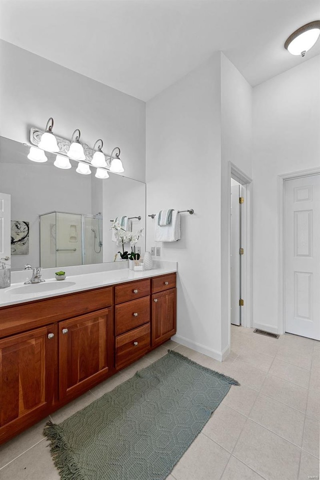 bathroom featuring double vanity, a stall shower, a sink, baseboards, and tile patterned floors