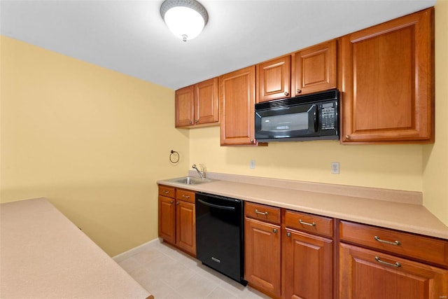 kitchen with a sink, black appliances, light countertops, and brown cabinets