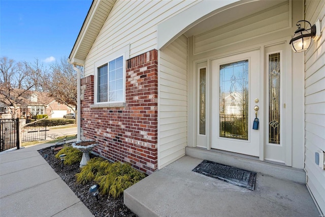 view of exterior entry featuring brick siding and fence