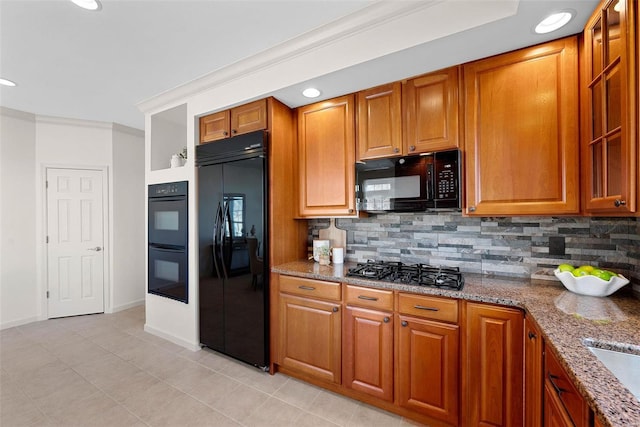 kitchen featuring black appliances, stone counters, brown cabinetry, and backsplash