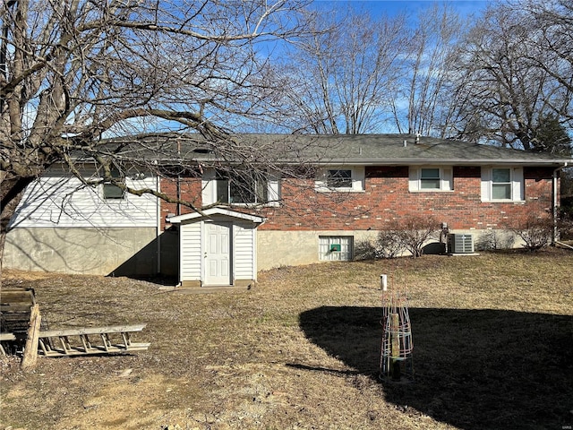 back of property with an outbuilding, brick siding, a lawn, central AC, and a shed