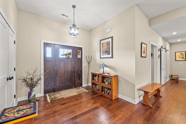 entryway with visible vents, baseboards, a barn door, hardwood / wood-style floors, and an inviting chandelier