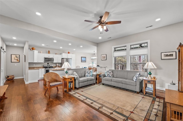 living area with baseboards, a barn door, recessed lighting, ceiling fan with notable chandelier, and hardwood / wood-style flooring