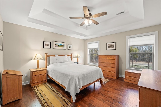 bedroom with visible vents, dark wood-type flooring, baseboards, a raised ceiling, and a ceiling fan