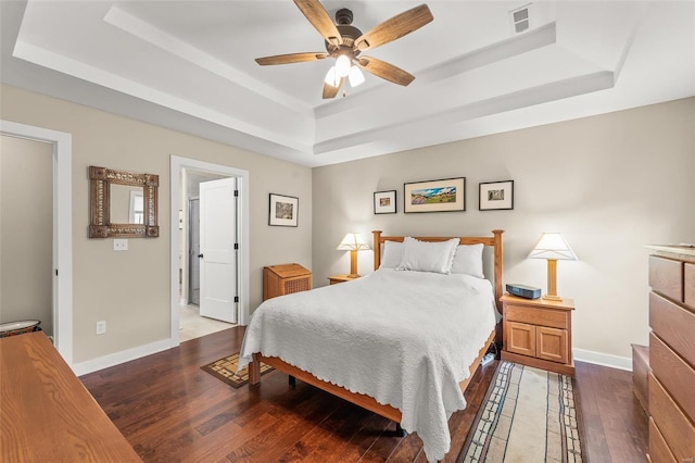 bedroom featuring visible vents, a ceiling fan, a tray ceiling, wood-type flooring, and baseboards