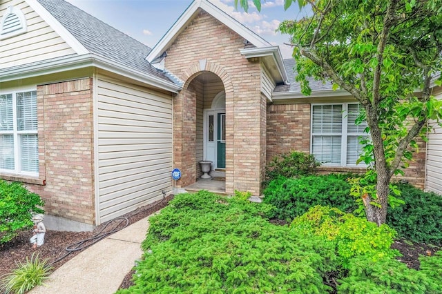 entrance to property with brick siding and a shingled roof