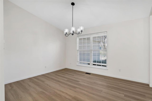 empty room featuring an inviting chandelier, wood finished floors, baseboards, and visible vents