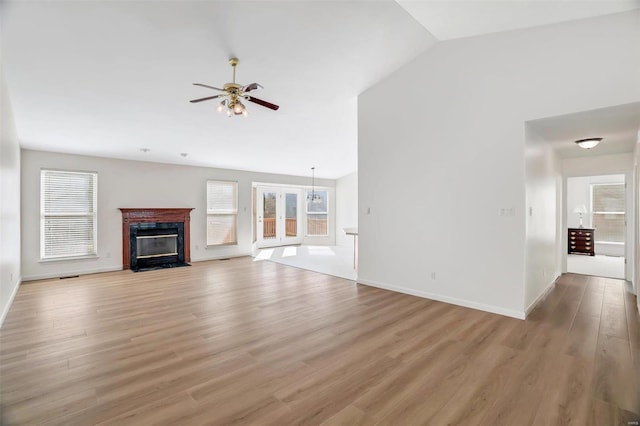 unfurnished living room featuring vaulted ceiling, a fireplace with flush hearth, light wood-style floors, and plenty of natural light