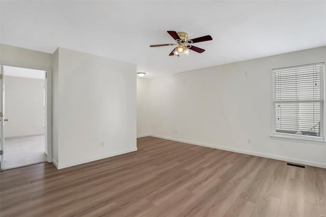 spare room with light wood-type flooring, baseboards, visible vents, and a ceiling fan