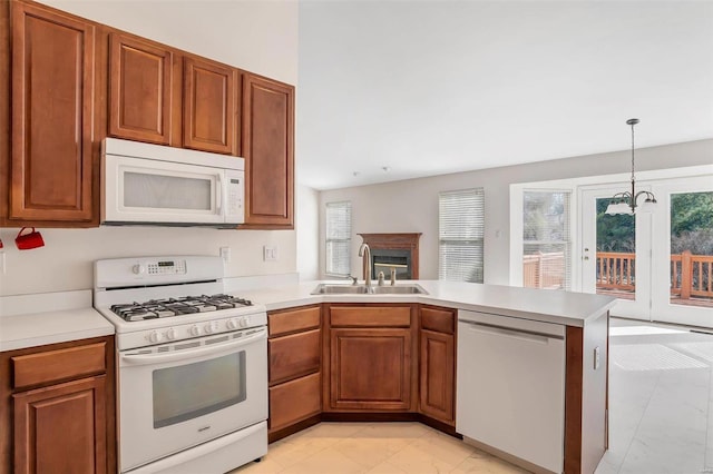 kitchen with light countertops, a peninsula, brown cabinetry, white appliances, and a sink