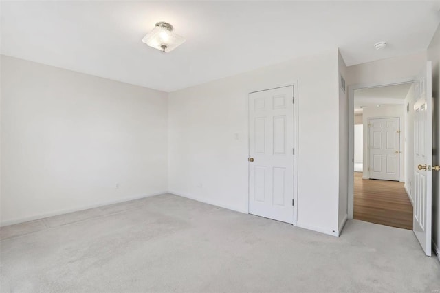 spare room with baseboards and light colored carpet