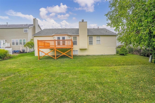 back of property with a yard, a wooden deck, a chimney, and fence