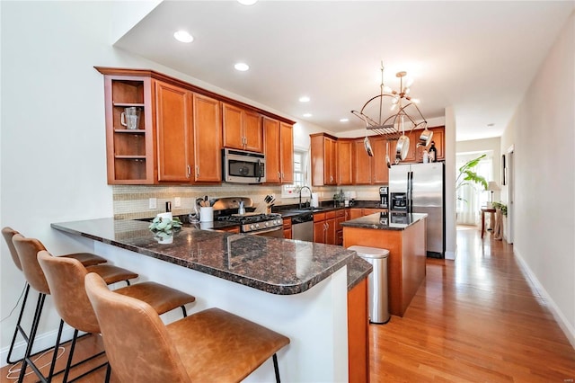 kitchen featuring brown cabinetry, a peninsula, a sink, stainless steel appliances, and backsplash