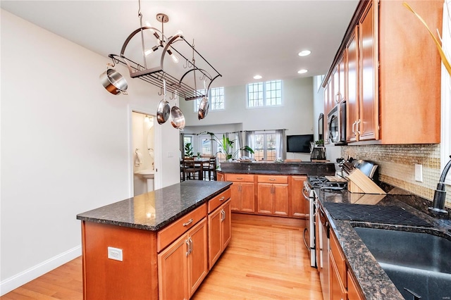 kitchen with brown cabinets, decorative backsplash, appliances with stainless steel finishes, light wood-style floors, and a sink