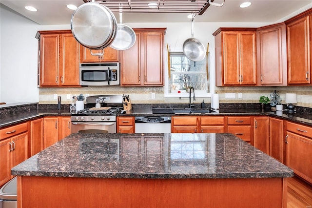 kitchen featuring a kitchen island, a sink, appliances with stainless steel finishes, tasteful backsplash, and dark stone countertops