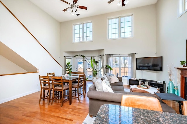 living room featuring baseboards, a ceiling fan, a towering ceiling, light wood-style flooring, and a fireplace