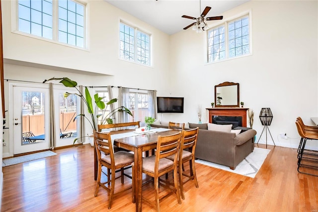 dining area with a towering ceiling, light wood-style floors, a fireplace, and a ceiling fan