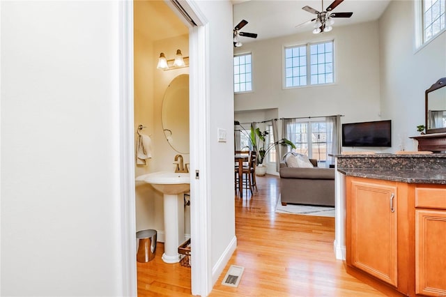 hall featuring a towering ceiling, light wood finished floors, baseboards, and visible vents