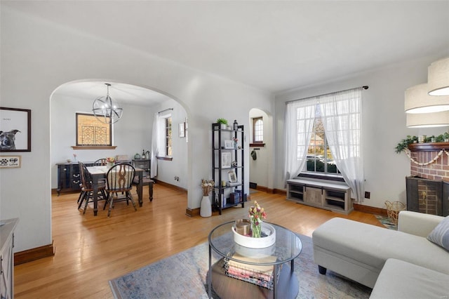 living room featuring light wood-style floors, baseboards, arched walkways, and an inviting chandelier