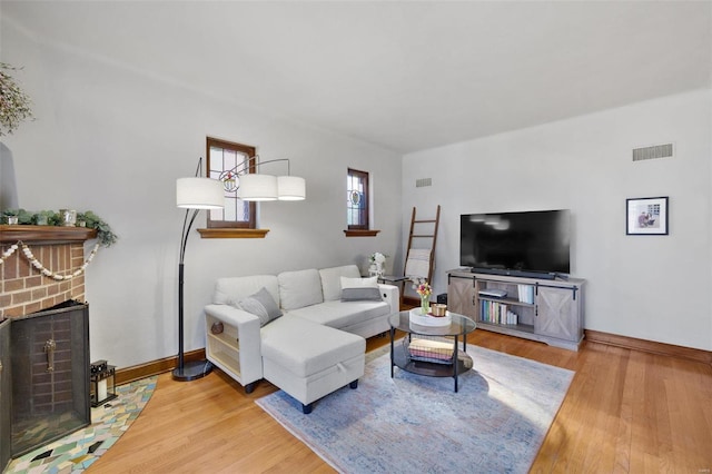 living room featuring baseboards, a fireplace, visible vents, and wood finished floors