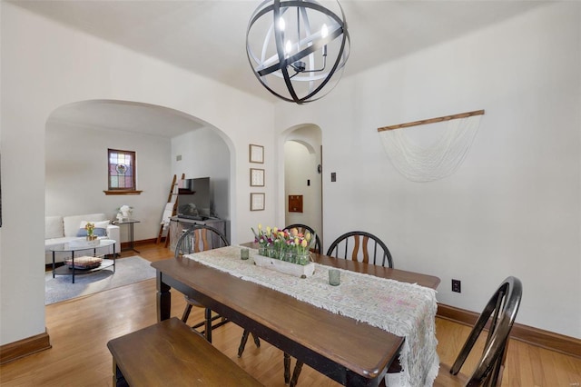 dining room featuring a chandelier, arched walkways, light wood-style flooring, and baseboards