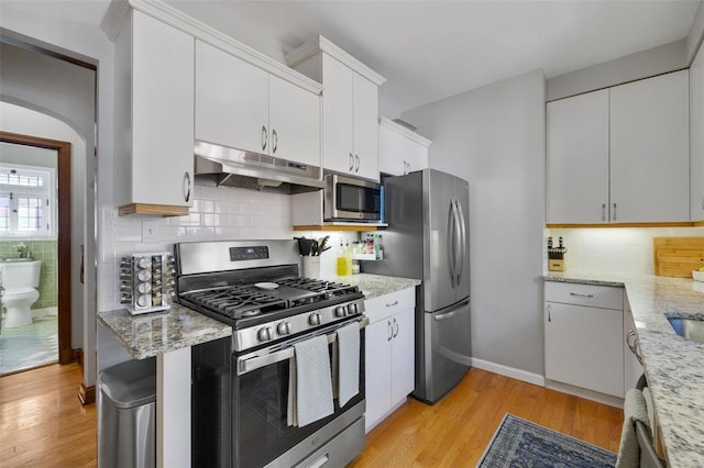 kitchen featuring tasteful backsplash, white cabinets, light wood-style floors, appliances with stainless steel finishes, and under cabinet range hood