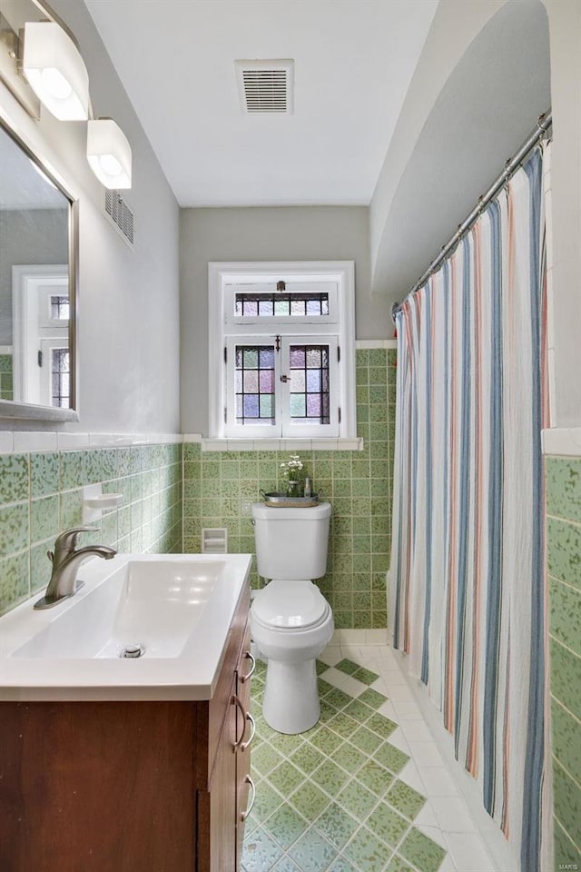 bathroom with toilet, vanity, visible vents, and tile walls