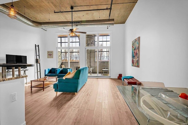 living area featuring ceiling fan, a high ceiling, visible vents, and hardwood / wood-style floors