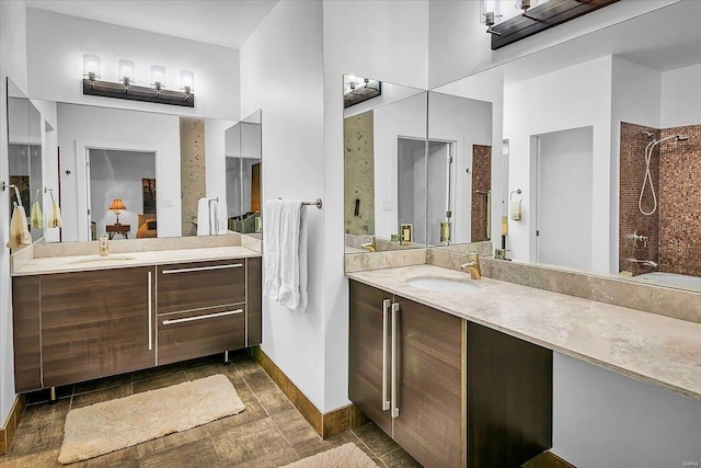 full bathroom featuring a shower, two vanities, a sink, and baseboards