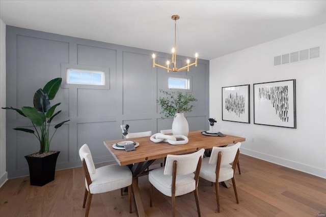 dining room featuring light wood finished floors, baseboards, visible vents, an inviting chandelier, and a decorative wall