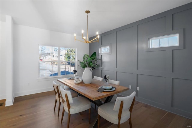 dining space with baseboards, a decorative wall, an inviting chandelier, and wood finished floors