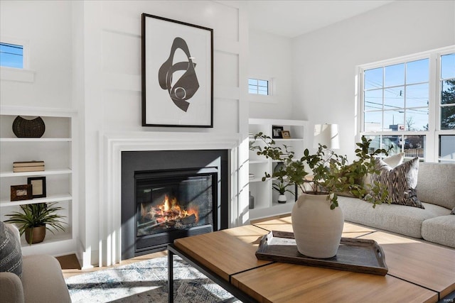 living room featuring built in features, a glass covered fireplace, and wood finished floors