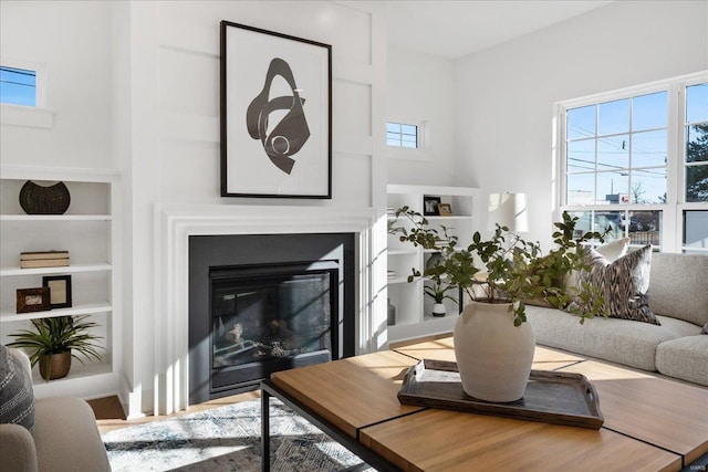 living area with built in features, wood finished floors, and a glass covered fireplace