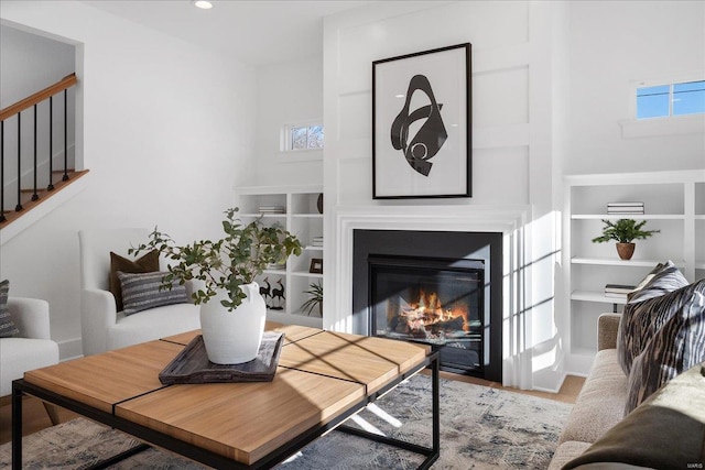 living area with stairs, recessed lighting, a glass covered fireplace, and a healthy amount of sunlight