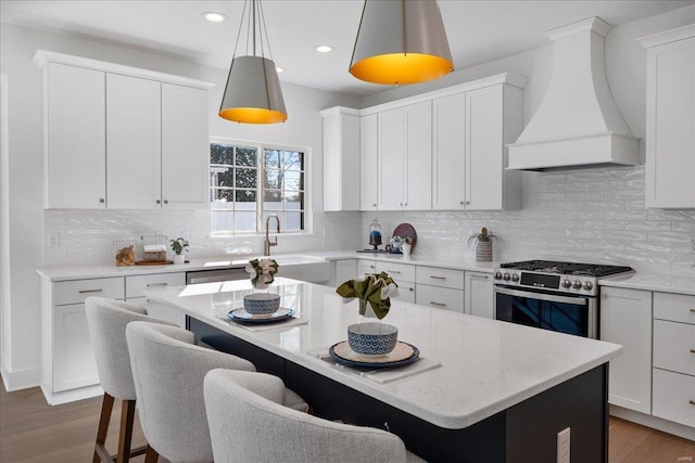 kitchen featuring white cabinets, a breakfast bar, a center island, premium range hood, and gas stove