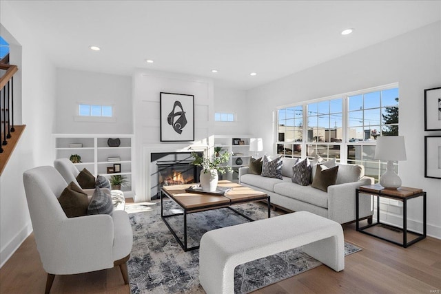 living area featuring recessed lighting, a glass covered fireplace, wood finished floors, baseboards, and stairs